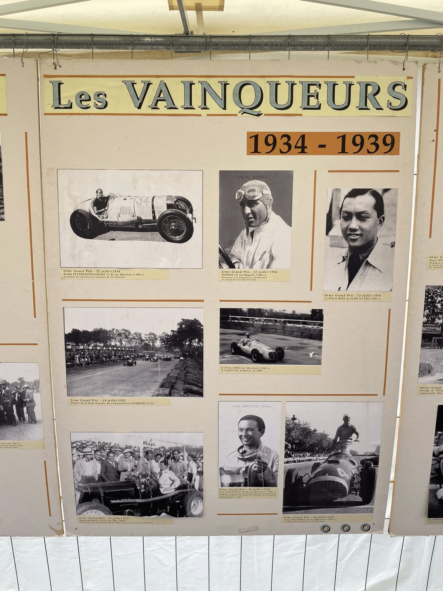 Panneau d'exposition Les Vainqueurs 1934-1939 avec photos de pilotes et voitures anciennes.